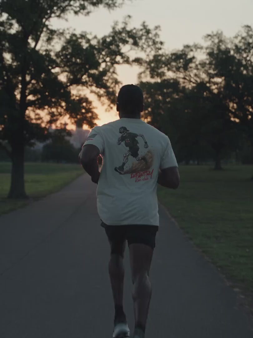 Black male runner in a cap and sports glasses sprinting at dawn in the Sand Infantry Run Club T-shirt