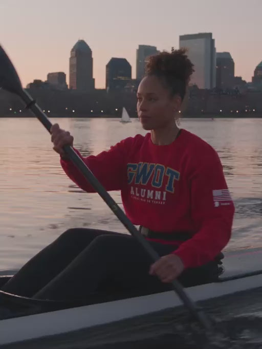Woman kayaking on the Charles River in Boston at sunset wearing the red GWOT Alumni crewneck
